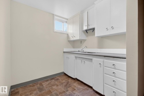 Kitchenette featuring white cabinetry, a double basin sink, and a window for natural light - 9740 65 Avenue Nw, Edmonton, AB 