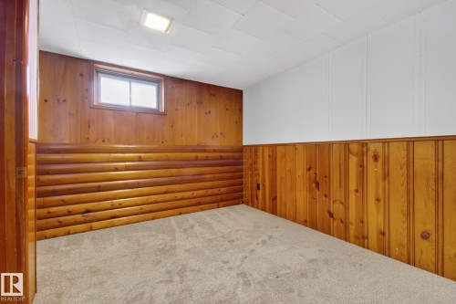 Carpeted room featuring natural wood paneling, a recessed window, and a ceiling light fixture - 9740 65 Avenue Nw, Edmonton, AB 