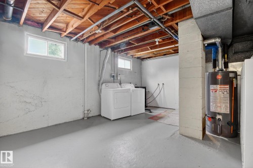 Spacious unfinished basement featuring exposed ceiling joists, concrete block walls, and painted concrete flooring - 9740 65 Avenue Nw, Edmonton, AB 