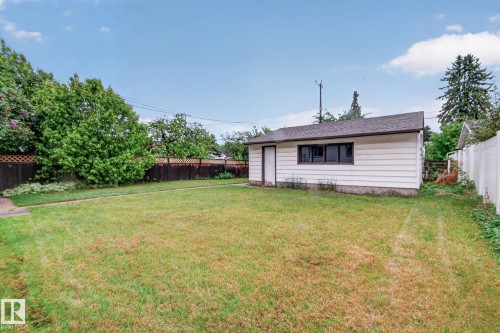 Detached garage with white siding, dark trim, and a shingled roof, set within a spacious grassy area - 9740 65 Avenue Nw, Edmonton, AB 