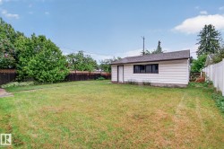 Detached garage with white siding, dark trim, and a shingled roof, set within a spacious grassy area - 