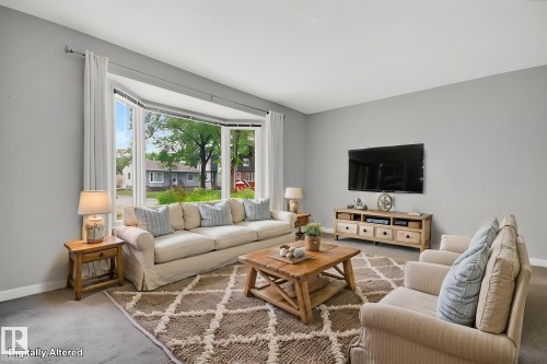 Spacious living area featuring a prominent bay window, light gray wall color, white trim, and carpeted flooring - 9740 65 Avenue Nw, Edmonton, AB 