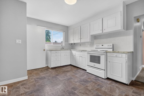 Kitchen featuring white cabinetry, light-toned countertops, a white electric range, and patterned flooring - 9740 65 Avenue Nw, Edmonton, AB 