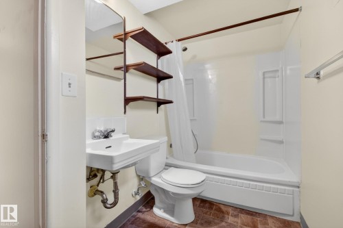 Bathroom featuring a white pedestal sink, toilet, and a white bathtub with an integrated shower - 9740 65 Avenue Nw, Edmonton, AB 
