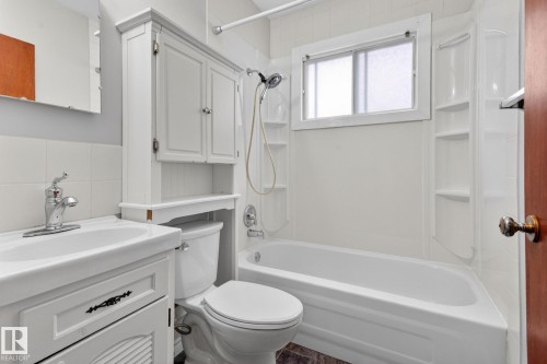 Full bathroom featuring a white vanity with integrated sink, chrome faucet, white over-toilet cabinet, and a white bathtub with a shower kit - 9740 65 Avenue Nw, Edmonton, AB 