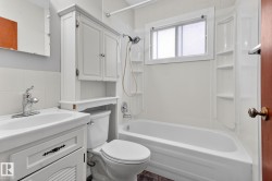 Full bathroom featuring a white vanity with integrated sink, chrome faucet, white over-toilet cabinet, and a white bathtub with a shower kit - 