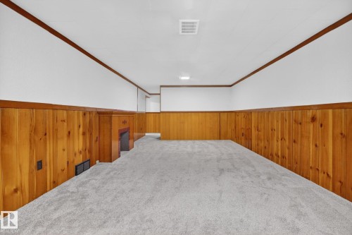 Spacious room featuring new grey carpeting, wood paneling, a white ceiling with recessed lighting, and a brick fireplace - 9740 65 Avenue Nw, Edmonton, AB 