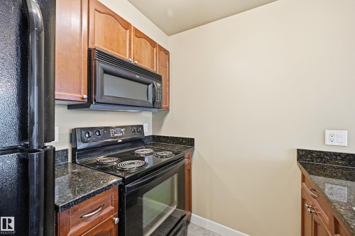 Kitchen featuring black appliances, granite countertops, wood-finish cabinetry, and an over-range microwave - 1407 9939 109 Street, Edmonton, AB 