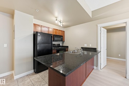 Kitchen featuring a dark granite-finish island with an undermount dual-basin sink and a black appliance suite - 1407 9939 109 Street, Edmonton, AB 