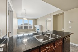 Kitchen island featuring a dual-basin stainless steel sink with chrome faucet, dark speckled countertop, and integrated dishwasher - 