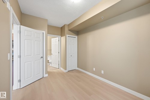 Spacious room featuring light wood-finish flooring, neutral wall paint, and white trim - 1407 9939 109 Street, Edmonton, AB 