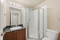 Corner shower enclosure with clear glass panels, white subway tile surround, dark wood-finish vanity with a stone-finish countertop, and a contemporary oval sink - 