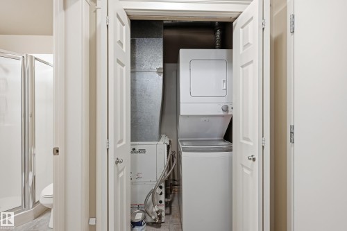 Dedicated utility closet featuring a stacked washer and dryer, adjacent to an HVAC system and water heater - 1407 9939 109 Street, Edmonton, AB 