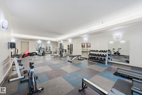 Fitness room featuring a variety of exercise equipment, wall-mounted mirrors, and recessed lighting - 1407 9939 109 Street, Edmonton, AB 