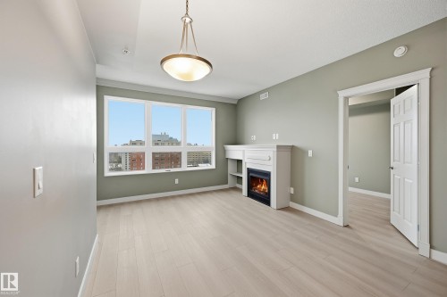 Spacious room featuring wood-finish flooring, a built-in fireplace with mantle and shelving, a multi-pane window, and an overhead decorative light fixture - 1407 9939 109 Street, Edmonton, AB 