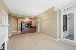 Light wood-finish flooring extending from the living area to the kitchen, featuring wood cabinetry and black appliances - 