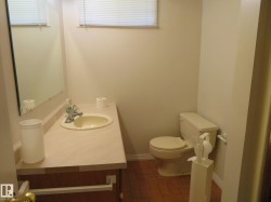 Bathroom featuring a vanity with an integrated sink, a rectangular mirror, a window with blinds, and brick-patterned flooring - 