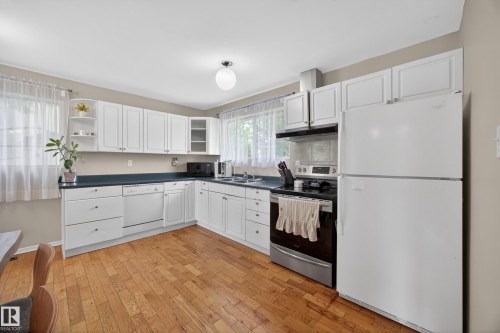 Kitchen featuring wood-finish flooring, white cabinetry, dark countertops, and stainless steel appliances including a range and refrigerator - 5216 104A Street, Edmonton, AB - Indoor Photo Showing Kitchen