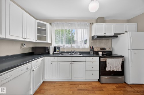 Kitchen featuring white cabinetry, dark countertops, wood-finish flooring, and a stainless steel and black range - 5216 104A Street, Edmonton, AB - Indoor Photo Showing Kitchen With Double Sink