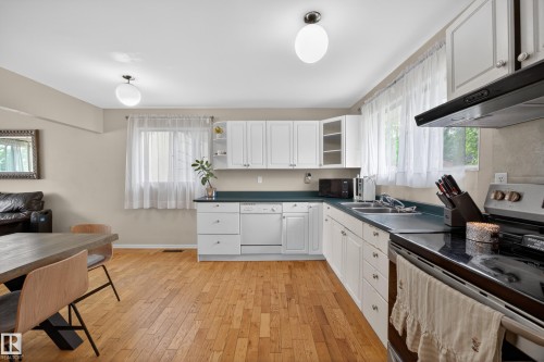 Open-concept kitchen featuring wood-finish flooring, white cabinetry, dark countertops, and stainless steel appliances - 5216 104A Street, Edmonton, AB - Indoor Photo Showing Kitchen With Double Sink