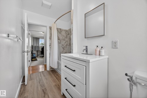 Bathroom featuring wood-finish flooring, a white vanity with black hardware, a rectangular sink, and a framed mirror - 5216 104A Street, Edmonton, AB - Indoor