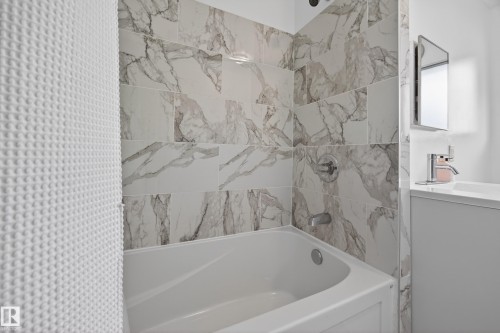 Tub and shower combination featuring large format marble-look wall tiles, chrome fixtures, and a white soaking tub - 5216 104A Street, Edmonton, AB - Indoor Photo Showing Bathroom
