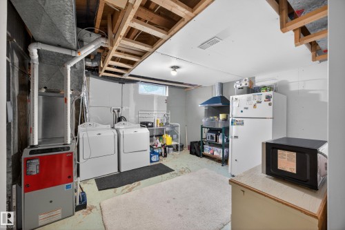Utility space featuring an exposed wood joist ceiling, a white washer and dryer, a red and gray furnace unit, and a window providing natural light - 5216 104A Street, Edmonton, AB - Indoor Photo Showing Laundry Room