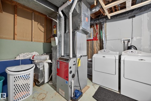 Dedicated utility area featuring a front-loading washing machine and dryer, a central heating unit, exposed ductwork, and unfinished walls - 5216 104A Street, Edmonton, AB - Indoor Photo Showing Laundry Room