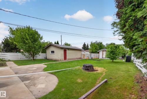 Spacious backyard featuring a stucco detached garage with a red door, a storage shed, a manicured lawn, and a white picket fence - 5216 104A Street, Edmonton, AB - Outdoor