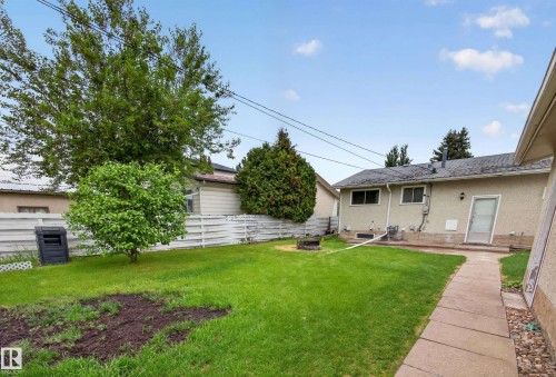 Expansive grassy yard featuring a concrete pathway, mature trees, a white picket fence, and a fire pit - 5216 104A Street, Edmonton, AB - Outdoor