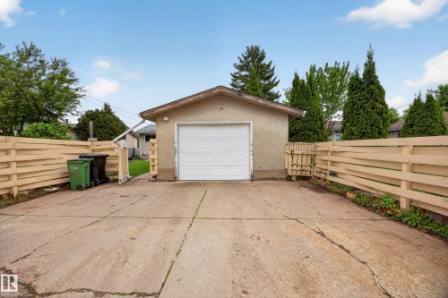 Detached garage with a white overhead door, concrete driveway, and light-toned wood fencing - 5216 104A Street, Edmonton, AB - Outdoor With Exterior