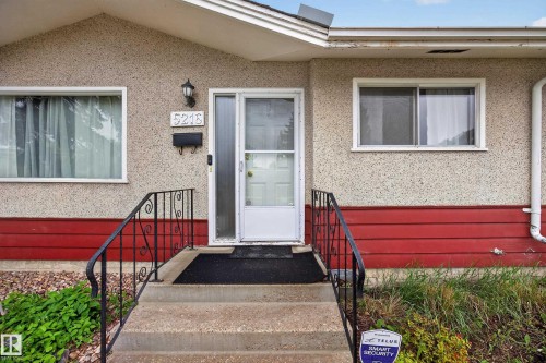 Front entry featuring concrete steps with wrought iron railing, a storm door, and decorative wall-mounted lighting - 5216 104A Street, Edmonton, AB - Outdoor With Exterior