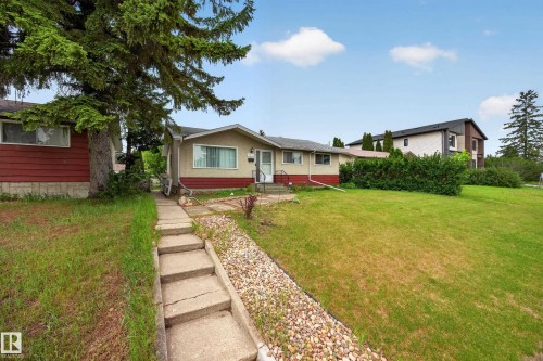 Single-story residence featuring light-colored siding with a contrasting red lower panel, a paved walkway with steps, a gravel garden bed, and a spacious front lawn - 5216 104A Street, Edmonton, AB - Outdoor