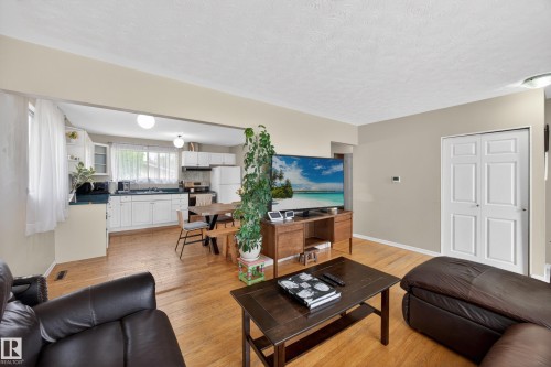 Open-concept living space featuring wood-finish flooring, a kitchen with white cabinetry, a built-in oven, and a double-door closet - 5216 104A Street, Edmonton, AB - Indoor Photo Showing Living Room