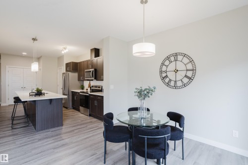 Open-concept kitchen and dining area featuring wood-finish flooring, dark wood cabinetry, stainless steel appliances, a kitchen island with a light-toned countertop, and a drum pendant light fixture - 9142 Pear Drive, Edmonton, AB - Indoor Photo Showing Dining Room