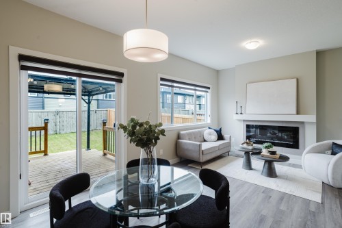 Open-concept living space with wood-finish flooring, a contemporary fireplace with mantel, and a sliding glass door providing direct access to an outdoor deck and backyard - 9142 Pear Drive, Edmonton, AB - Indoor Photo Showing Living Room With Fireplace