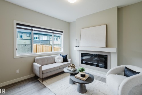 Living area featuring a modern linear fireplace with a mantle, large window, wood-finish flooring, and neutral wall tones - 9142 Pear Drive, Edmonton, AB - Indoor Photo Showing Living Room With Fireplace
