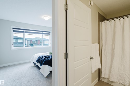 Carpeted room with a large window featuring roller shades, a flush mount ceiling light, and a white paneled door with a polished chrome doorknob - 9142 Pear Drive, Edmonton, AB - Indoor