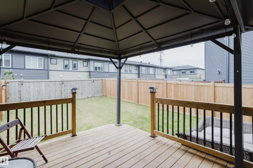 Covered patio deck with wood-finish flooring, black metal railing, and a fenced backyard featuring a manicured lawn - 9142 Pear Drive, Edmonton, AB - Outdoor With Deck Patio Veranda With Exterior