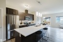 Modern kitchen featuring a spacious island with an undermount sink, pendant lighting, dark wood cabinetry, stainless steel appliances, and wood-finish flooring - 9142 Pear Drive, Edmonton, AB  - Indoor Photo Showing Kitchen With Double Sink With Upgraded Kitchen 