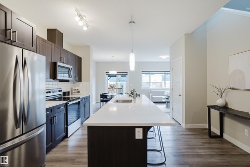 Modern kitchen featuring dark wood-finish cabinetry, stainless steel appliances, a white subway tile backsplash, and a large central island with a white countertop and integrated sink - 9142 Pear Drive, Edmonton, AB - Indoor Photo Showing Kitchen With Upgraded Kitchen