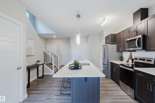 Contemporary kitchen featuring dark wood-finish cabinetry, stainless steel appliances, a white subway tile backsplash, and a central island with a white countertop and integrated sink - 9142 Pear Drive, Edmonton, AB - Indoor Photo Showing Kitchen With Upgraded Kitchen