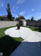 Expansive backyard featuring a circular concrete patio, a detached storage shed, and perimeter fencing - 
