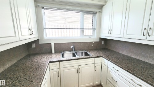 Kitchen featuring white cabinetry, a double basin stainless steel sink, speckled countertops, and a tiled backsplash - 8824 90 Street, Edmonton, AB 