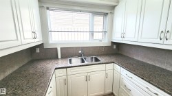 Kitchen featuring white cabinetry, a double basin stainless steel sink, speckled countertops, and a tiled backsplash - 