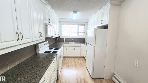 Galley-style kitchen featuring white cabinetry with brushed nickel hardware, laminate wood-finish flooring, dark speckled countertops, and a tiled backsplash - 8824 90 Street, Edmonton, AB 