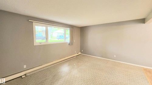 Spacious room featuring neutral grey walls and patterned carpet flooring - 8824 90 Street, Edmonton, AB 