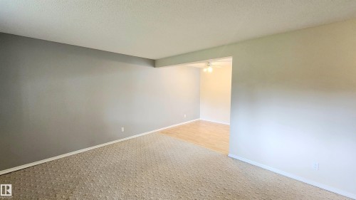 Neutral-toned carpeting with a geometric pattern, extending into a separate room featuring wood-finish flooring and a ceiling fan - 8824 90 Street, Edmonton, AB 