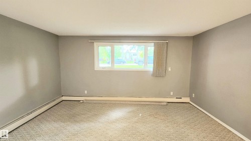 Spacious room featuring neutral grey walls and patterned carpet flooring - 8824 90 Street, Edmonton, AB 