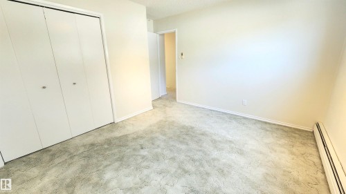 Interior room featuring neutral wall paint, light-toned carpet, white bi-fold closet doors, and baseboard heating - 8824 90 Street, Edmonton, AB 